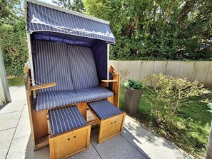 Un espace extérieur aménagé avec des sièges en bois, doté d’un coussin à rayures et d’un auvent.