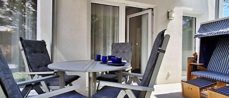 A patio with a round table and chairs, a grill, and a sliding glass door.