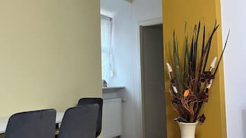 Un comedor con una mesa y sillas, un jarrón con plantas, y una puerta que da a otra habitación.