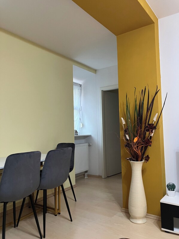 A dining area with a table and chairs, a vase with plants, and a door leading to another room.