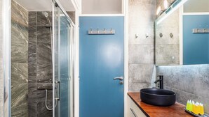 A bathroom with a glass shower enclosure, a blue door, a sink with a black basin, and a wooden countertop. - Modern 2BR Apartment in Limassol (Lemesos)