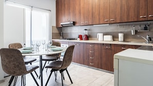 A modern kitchen with wooden cabinets, a dining table with chairs, and a window with blinds. - Modern 2BR Apartment in Limassol (Lemesos)