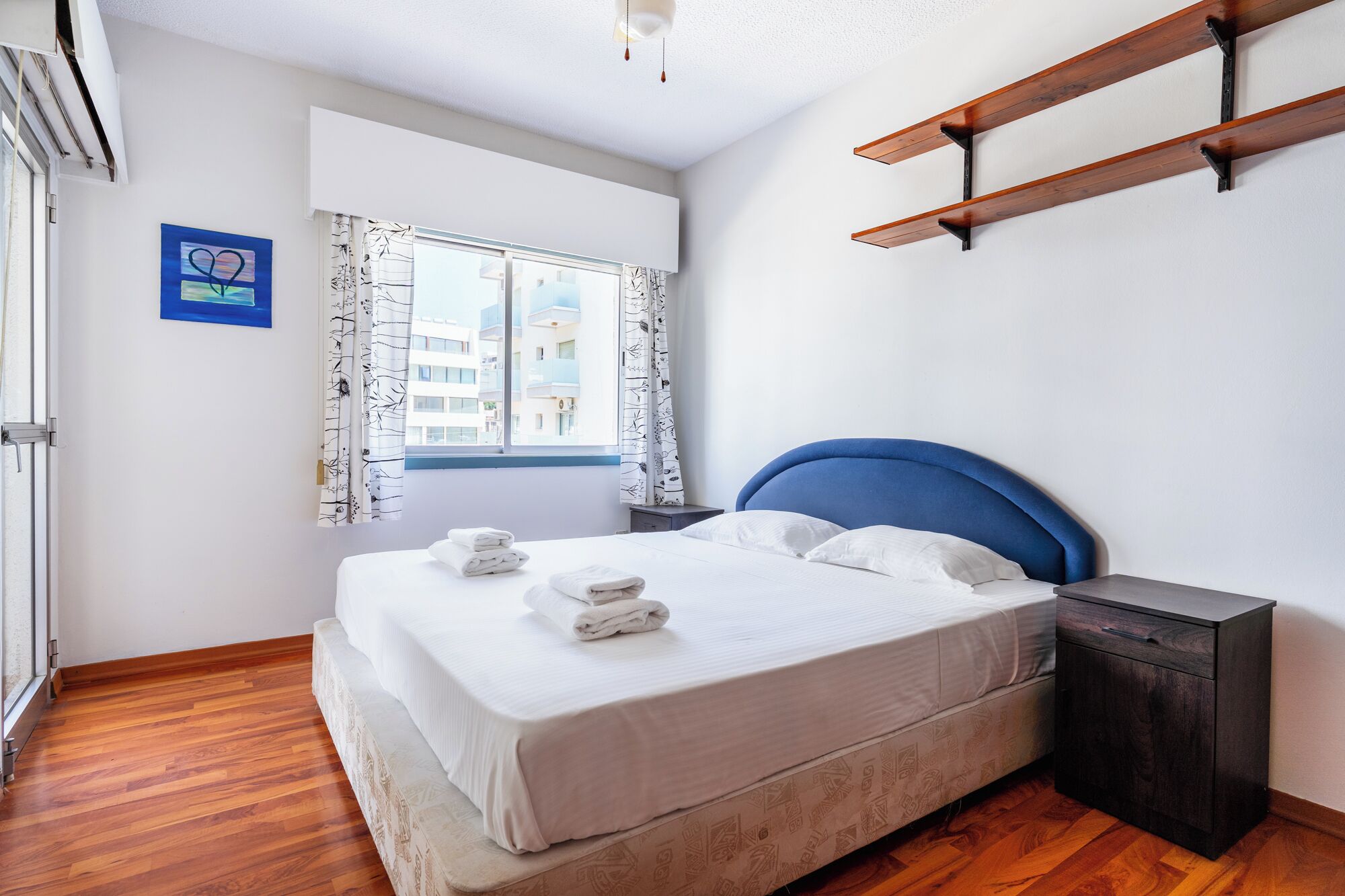 Una camera da letto con un letto, un comodino, una finestra con tende e una mensola a muro.
