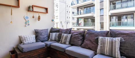 A modern outdoor seating area with a wooden bench and cushions, a coffee table with cups, and a wall with decorative items.