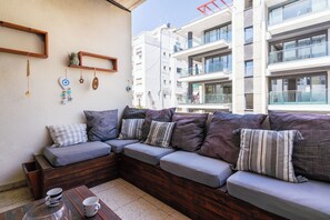 Un espace extérieur moderne aménagé avec un banc en bois et des coussins, une table basse avec des tasses, et un mur agrémenté d’objets décoratifs.