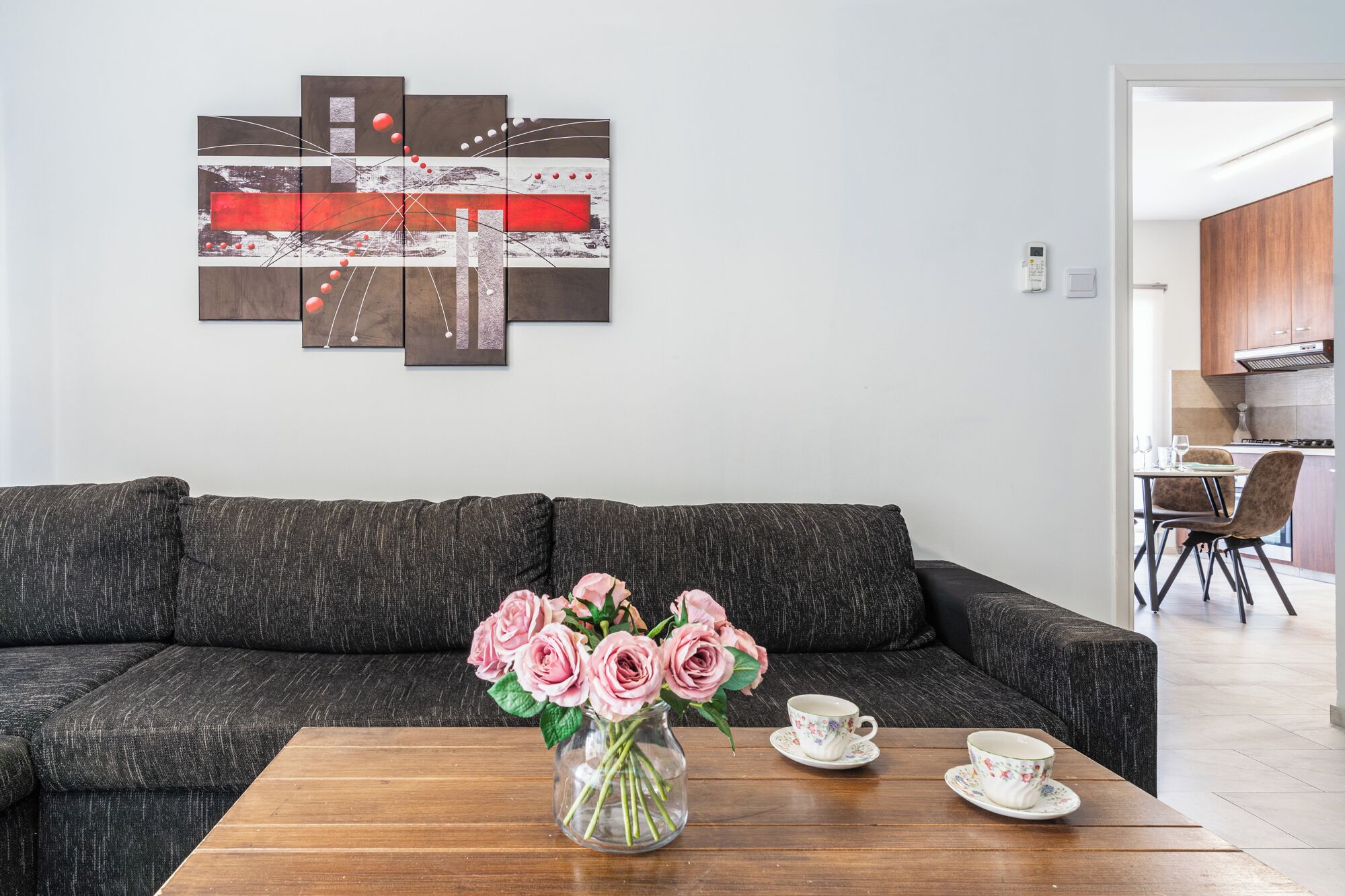 Un salon avec un canapé gris foncé, une table basse en bois, un vase contenant des roses roses, ainsi qu’une tasse et une soucoupe à thé décorées de motifs floraux.
