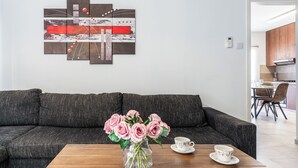Una sala de estar con un sofá gris oscuro, una mesa de centro de madera, un florero con rosas rosadas, y una taza y platillo con motivos florales.