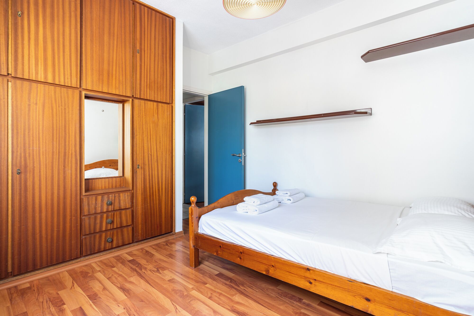 A bedroom with a wooden wardrobe, a single bed, and a blue door.