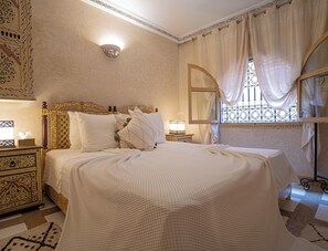 Een hotelkamer met een groot bed, een versierd hoofdbord en een decoratieve wandlamp.