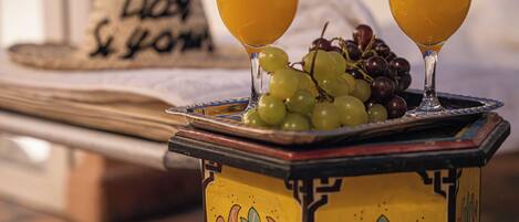 A table with two glasses of orange juice, a plate of grapes, and a decorative hat with text.