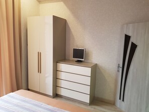 Ein Schlafzimmer mit Bett, Kleiderschrank, Schreibtisch und Computerbildschirm sowie einer Tür.