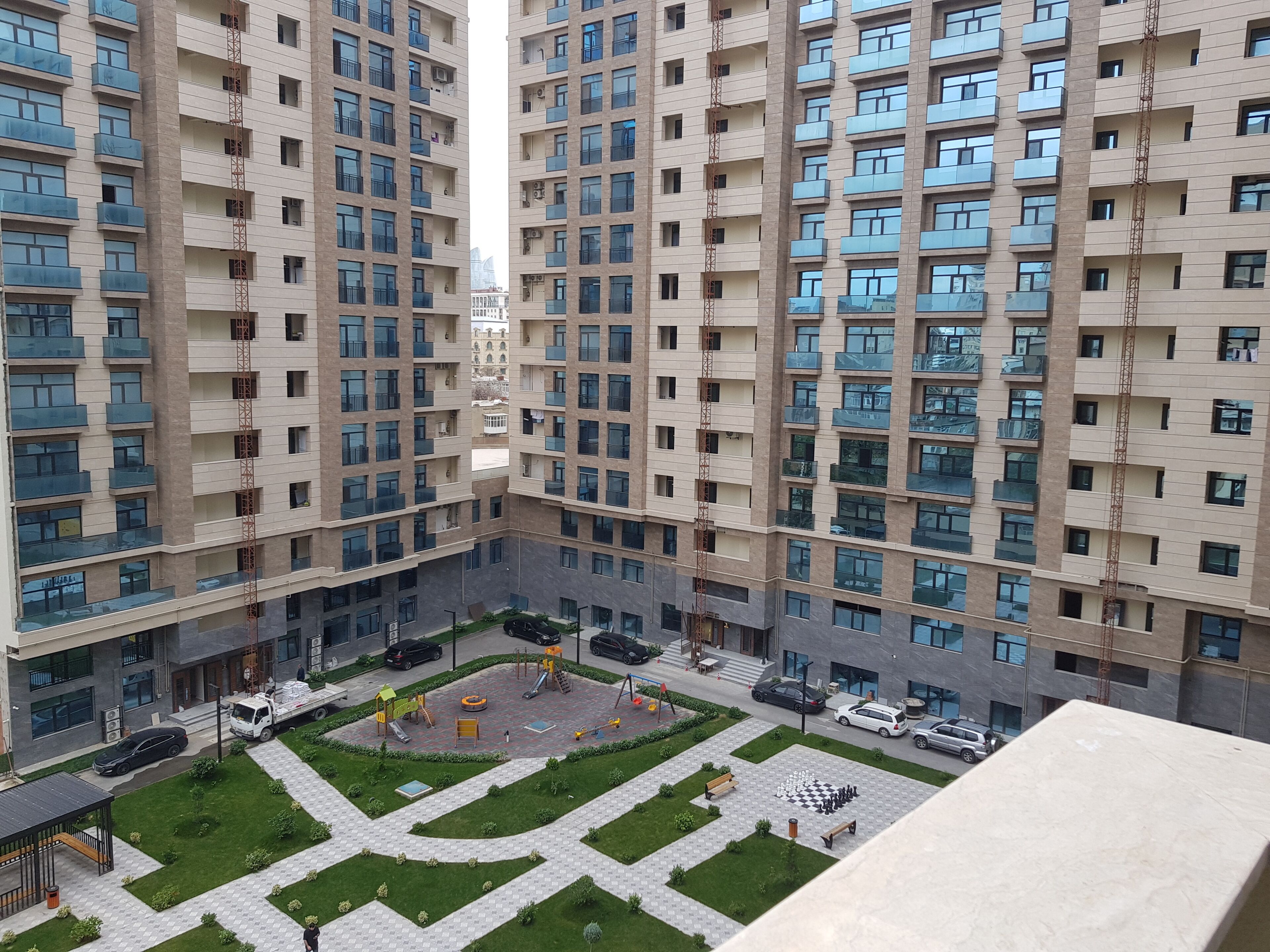A high-rise residential building with multiple balconies, a playground, and a parking area.