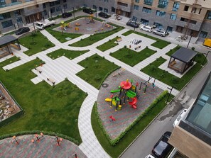 A playground with various play structures surrounded by a paved area with benches and a small garden. - Cozy 1-bedroom apartment in the Baku center (Bakı)