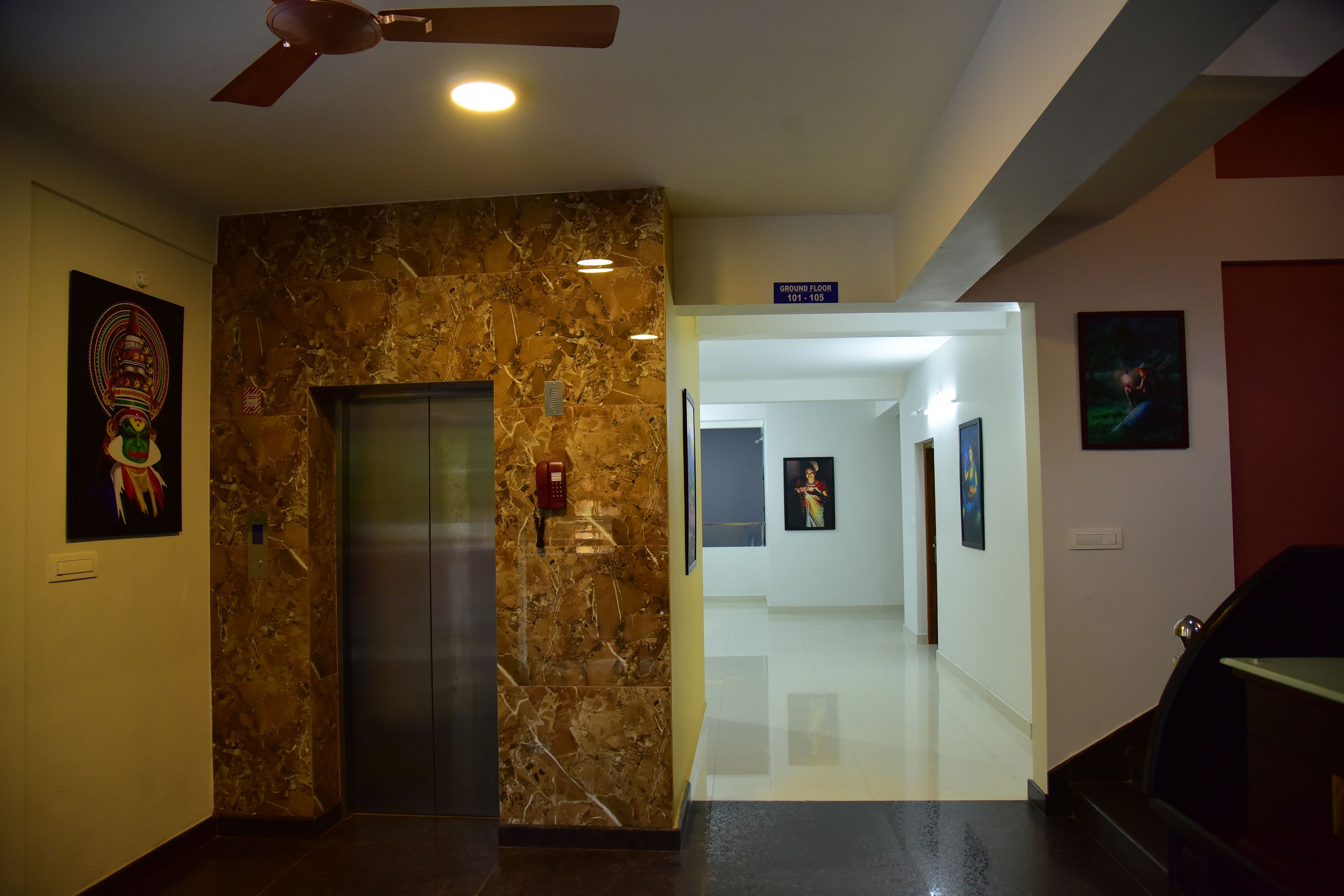 A hotel lobby with a marble wall, an elevator, and a hallway leading to the ground floor.