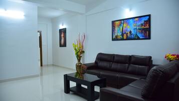 A modern living room with a black leather sofa, a glass coffee table, and a painting on the wall.