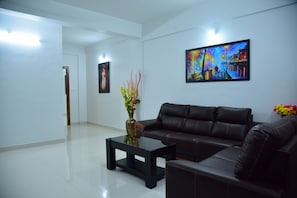 A modern living room with a black leather sofa, a glass coffee table, and a painting on the wall. - Dreamz Residency (Edava)