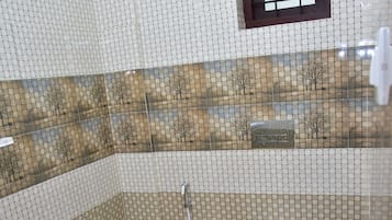 Un baño con piso de azulejos, inodoro, zona de ducha con puerta de vidrio y ventana con vista a árboles.