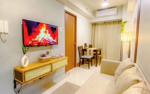 Uma sala de estar com televisão de tela plana, um rack de madeira, um espaço de jantar com mesa e cadeiras, e um sofá.