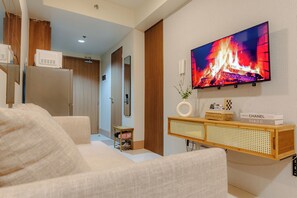 A modern living room with a flat-screen TV mounted on the wall, a wooden cabinet with a woven basket, and a sofa. - Shore 3 Bay City Suites 1BR Netflix + WiFi near MOA, NAIA, SMX (Pasay City)