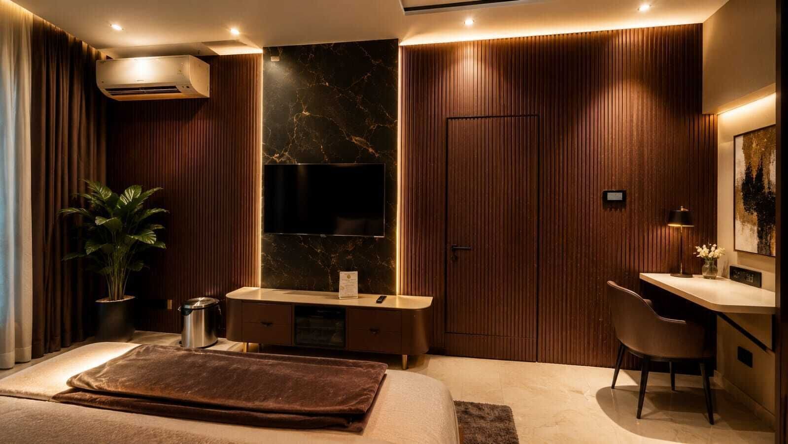 A modern bedroom with a large bed, a bedside table, a desk, a chair, a potted plant, and a wall-mounted TV.