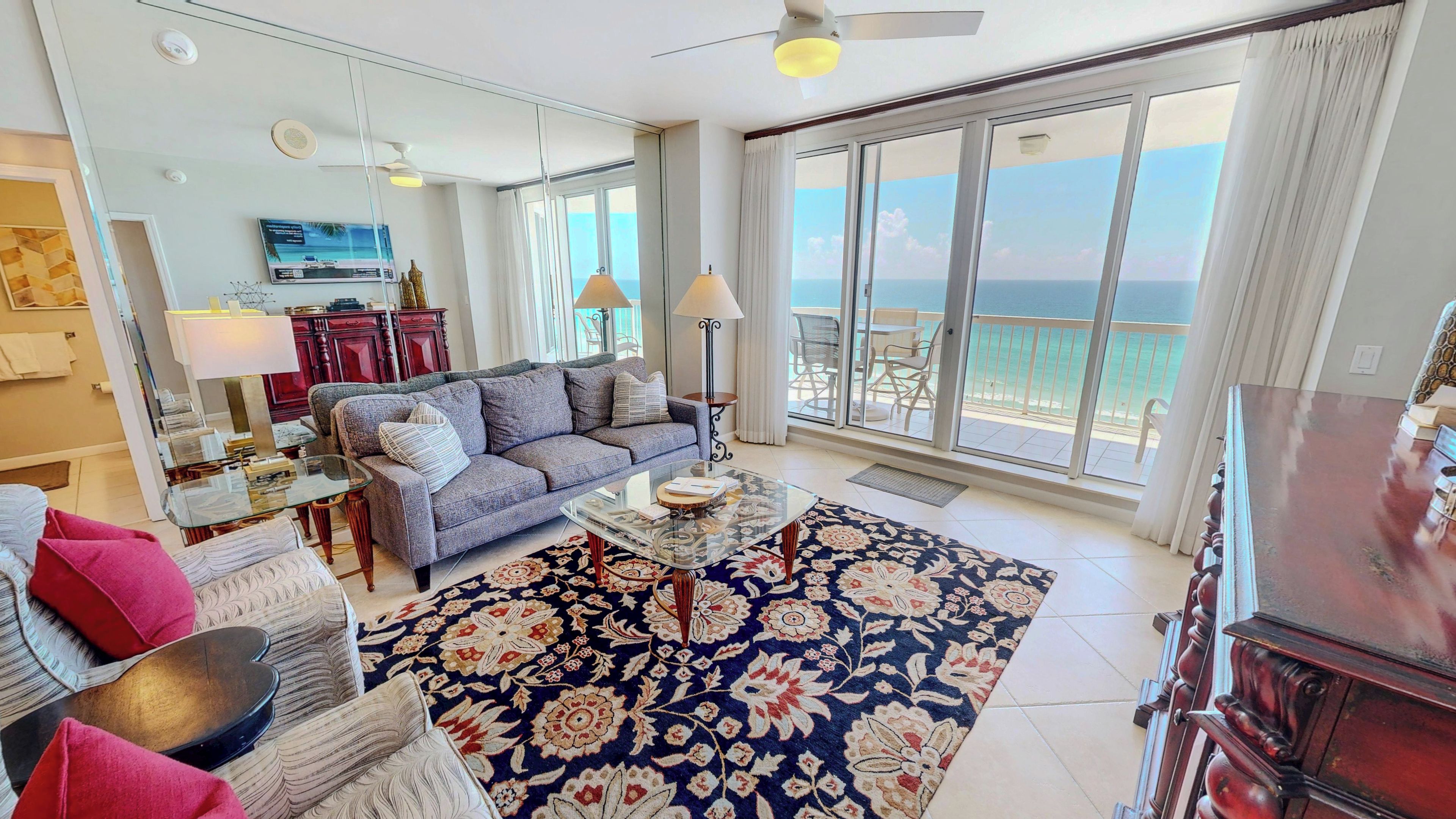 A spacious living room with a large window overlooking the sea, a sofa, a coffee table, and a red cabinet.