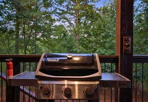 Ein Weber Spirit II Grill steht auf einer Terrasses mit Holzgeländer, links daneben ein Feuerlöscher.