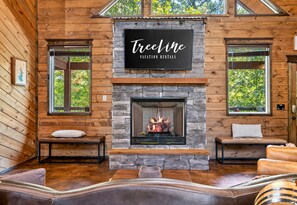 Ein Interieur einer Blockhütte mit Kamin aus Stein, zwei Bänken und einem Schild über dem Kamin mit der Aufschrift 'TreeLine Vacation Rentals'.