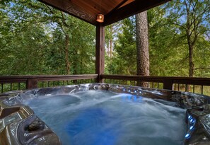 Ein Whirlpool auf einer Holzterrasse, umgeben von Bäumen.
