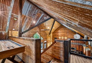A rustic wooden interior with a sloped ceiling, a wooden table, and a staircase leading to an upper level. - Game Loft | Hot Tub | Fire Pit | Boat Parking (Broken Bow)