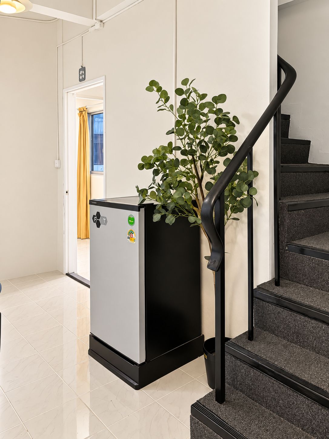 A modern interior with a staircase, a grey appliance, and a potted plant.