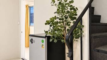 A modern interior with a staircase, a grey appliance, and a potted plant.
