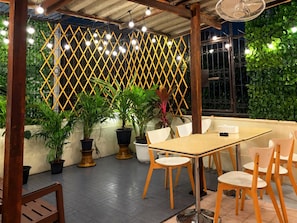 An outdoor patio area with a table and chairs, potted plants, and a decorative yellow lattice wall. - Charoennakhon 14 (Krung Thep Maha Nakhon)
