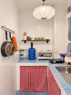 A kitchen with a blue countertop, a large blue water dispenser, a hanging pot rack, and a white ceiling light. - Charoennakhon 14 (Krung Thep Maha Nakhon)
