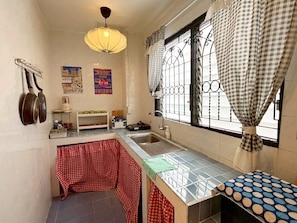 A compact kitchen with a sink, a hanging light fixture, and a window with metal bars and checkered curtains. - Charoennakhon 14 (Krung Thep Maha Nakhon)