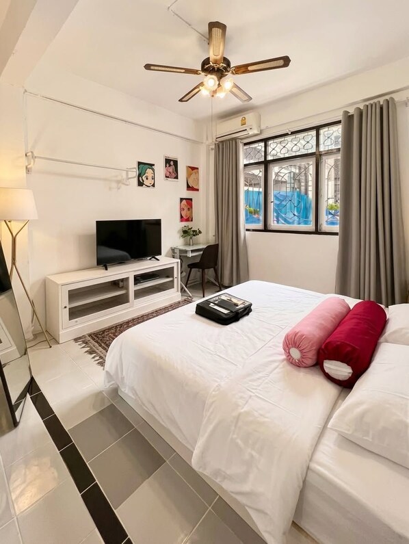 A hotel room with a bed, a TV on a white cabinet, a desk with a chair, and a window with curtains. - Charoennakhon 14 (Krung Thep Maha Nakhon)