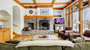A cozy living room with a stone fireplace, wooden beams, a television, and leather sofas.