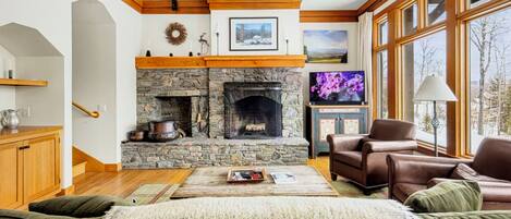 Una sala de estar acogedora con chimenea de piedra, vigas de madera, un televisor y sofás de cuero.