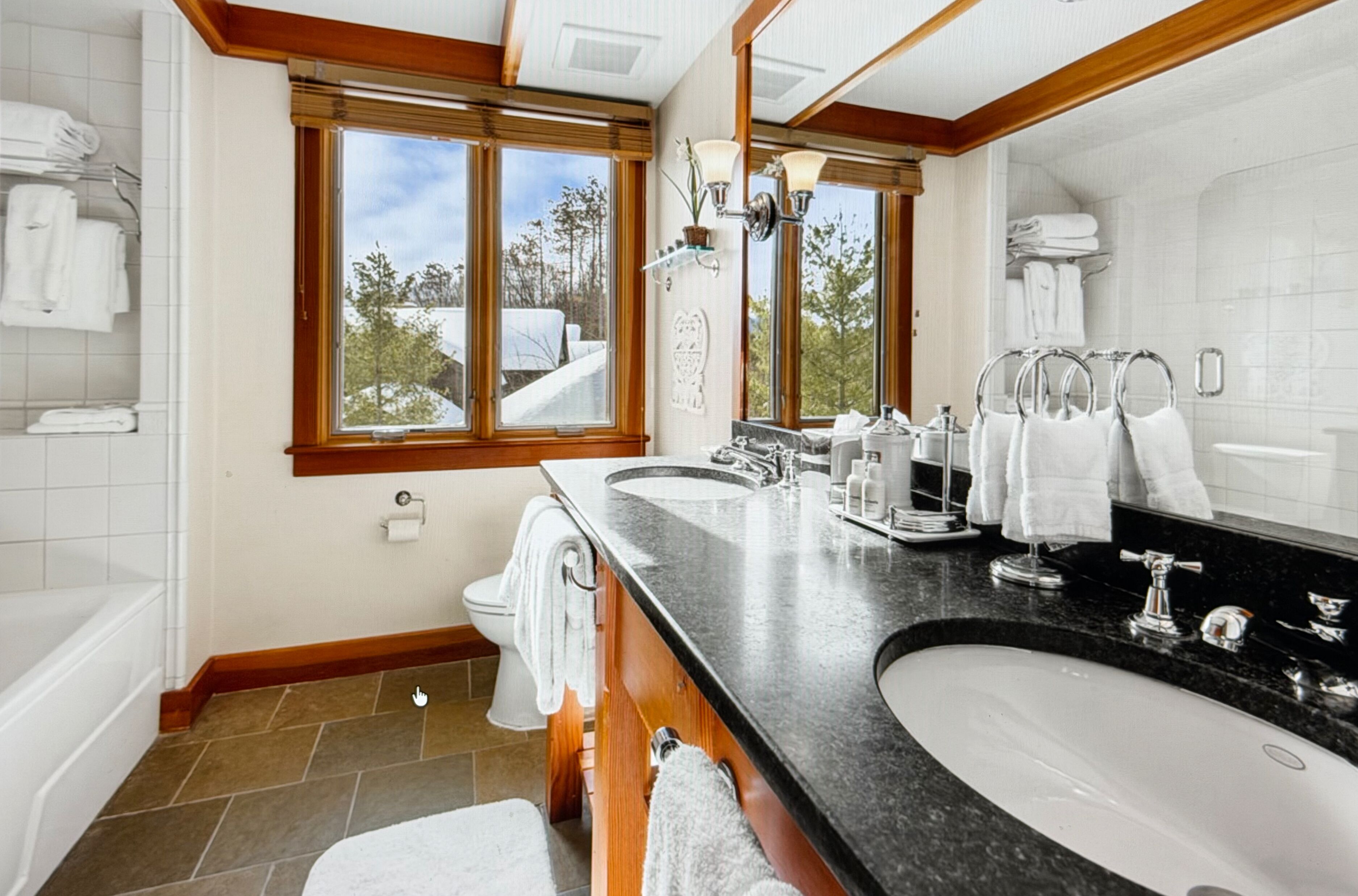 A bathroom with a large window, a double sink, and a bathtub.