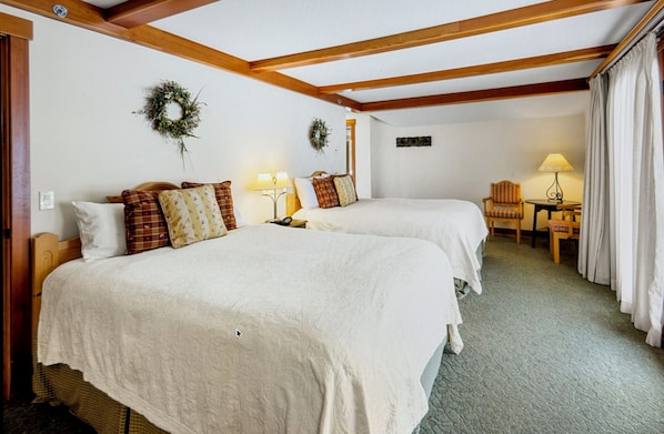 A hotel room with two beds, a small table, a chair, and a lamp.