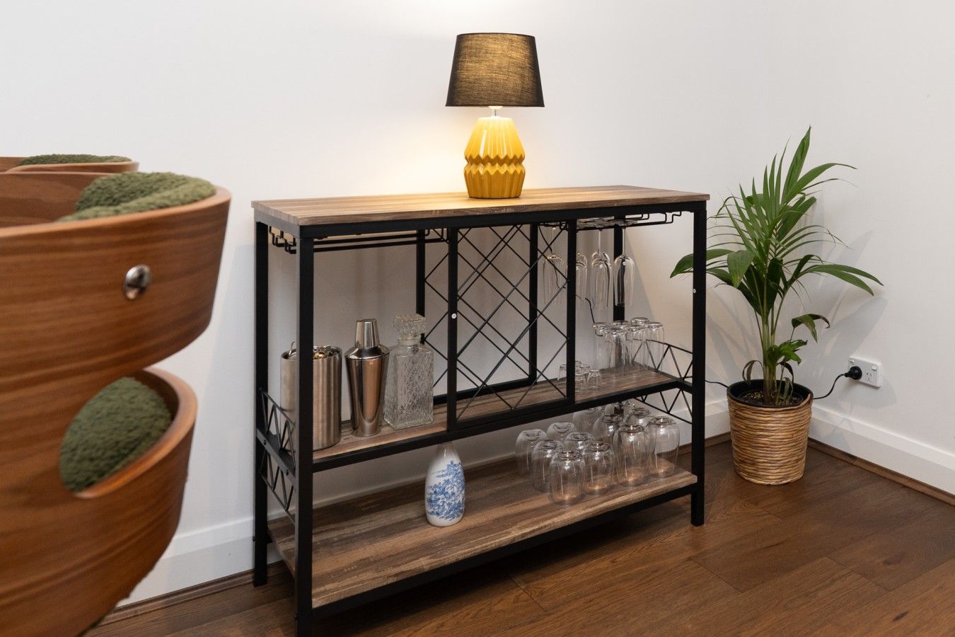 A wooden console table with a lamp, glassware, and a potted plant.