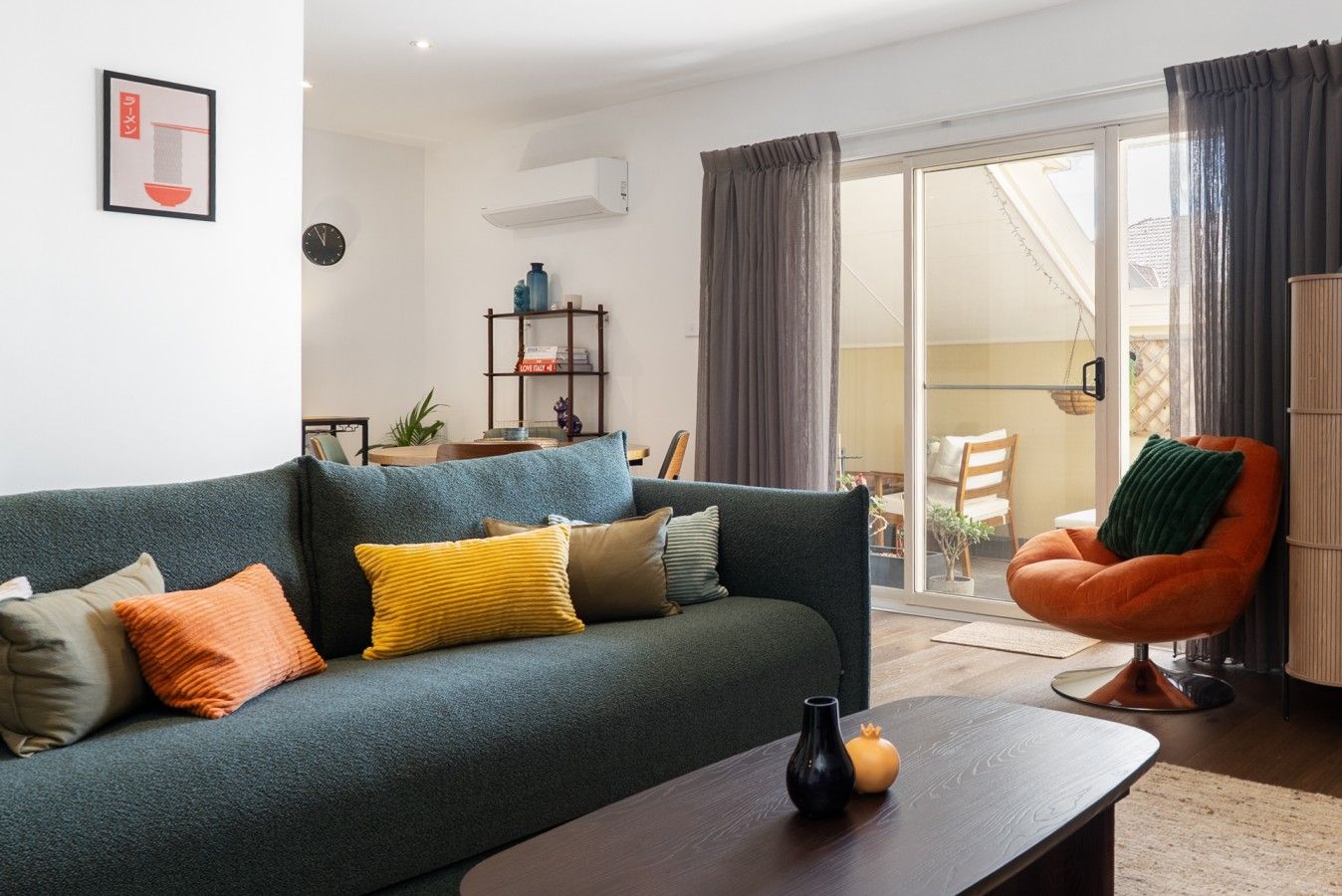 A modern living room with a sofa, a coffee table, and a chair. There is a bookshelf and a potted plant in the background.