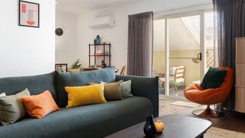 A modern living room with a sofa, a coffee table, and a chair. There is a bookshelf and a potted plant in the background.
