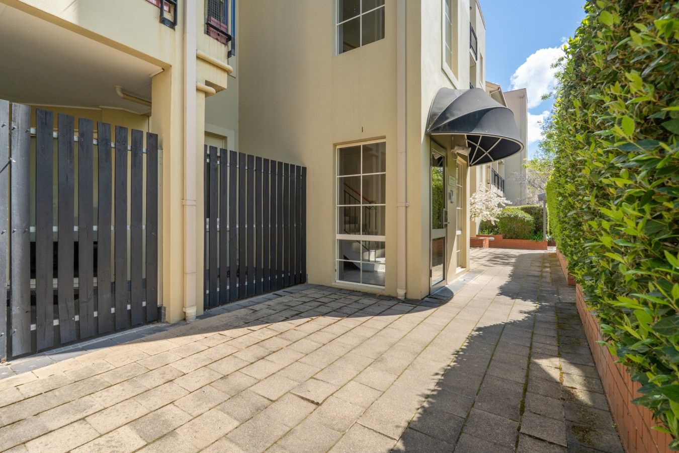 A paved courtyard with a black gate, a building entrance, and a covered outdoor area.