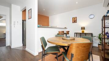 A modern kitchen with wooden cabinets, a built-in oven, and a dining area with a round wooden table and green upholstered chairs.