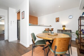 A modern kitchen with wooden cabinets, a built-in oven, and a dining area with a round wooden table and green upholstered chairs. - Eclectic 1BR With Private Terrace Near Manuka (Forrest)