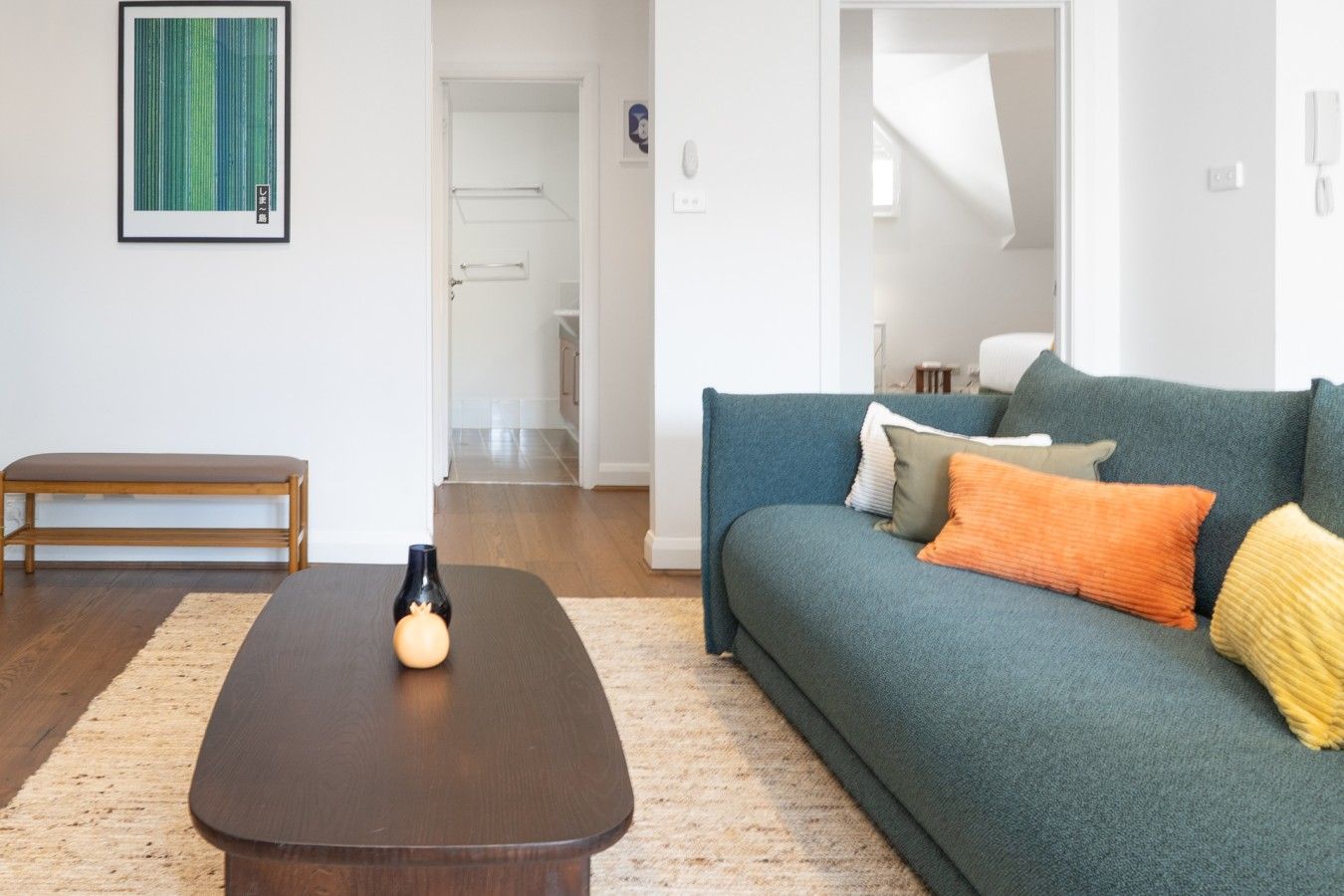 Een woonkamer met een donkerbruine salontafel, een smaragdgroene bank met kleurrijke kussens en een houten bankje.