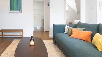 Een woonkamer met een donkerbruine salontafel, een smaragdgroene bank met kleurrijke kussens en een houten bankje.