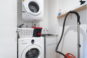 Ein Waschraum mit einer Waschmaschine mit Frontlader, einem Trockner mit Oberlader, einem Waschbecken und einem Schlauch.