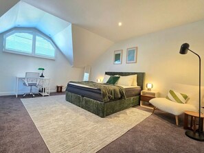 Ein Schlafzimmer mit Bett, Schreibtisch, Stuhl, Stehlampe und einem Fenster mit Jalousien.