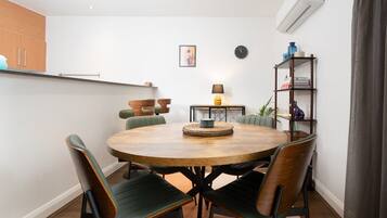 Un comedor con una mesa redonda de madera, cuatro sillas, una lámpara y una estantería.